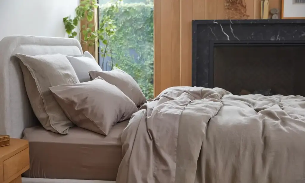 Sonnendurchflutetes Schlafzimmer mit einem Bett mit Leinenbettwäsche und einer dünnen weißen Baumwolldecke, die ein frisches und luftiges Gefühl vermitteln.