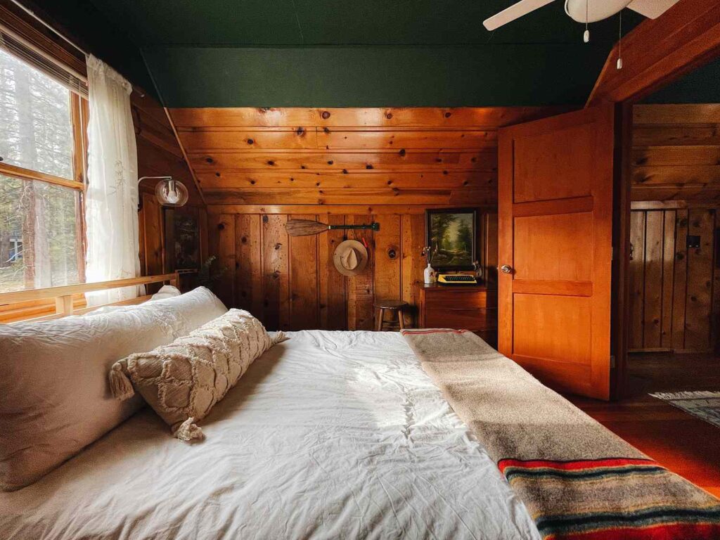 Lit accueillant habillé d'une literie de style lodge avec des couches de courtepointes et d'oreillers dans des tons terreux, situé dans une chambre à thème de cabane rustique.