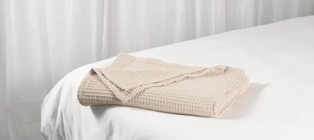 Lightweight white cotton waffle-weave blanket neatly folded on a bed in a sunlit room