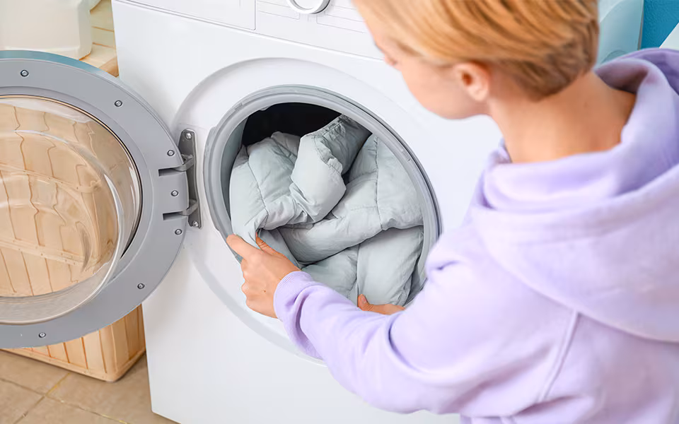 Person carefully placing a grey weighted blanket into a front-load washing machine for gentle cleaning