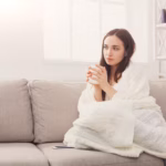 someone comfortably wrapped in a blanket on a sofa with a book and a warm drink.